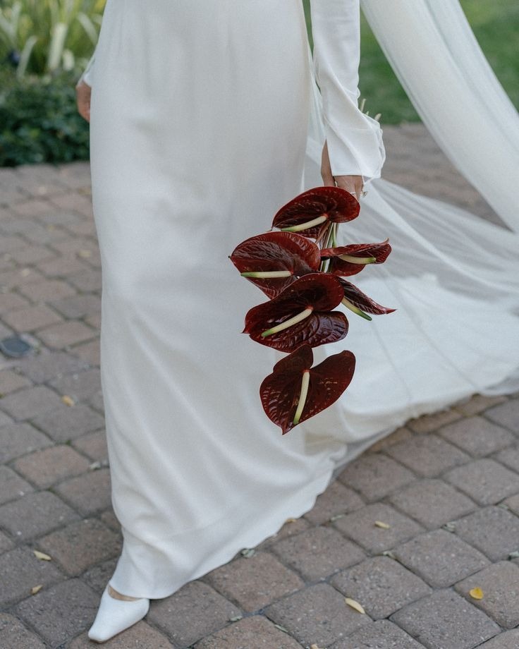 Novia con vestido blanco llevando un ramo estilizado de anturios borgoña